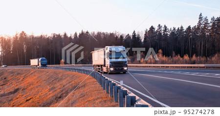 Trucks on the road with special trailers for the transport of bulk cargo of grain, crushed stone and sand against the background of the forest. Increased load capacity, industry Trucks on the road with special trailers for the transport of bulk cargo of grain, crushed stone and sand against the background of the forest. Increased load capacity, industry 95274278