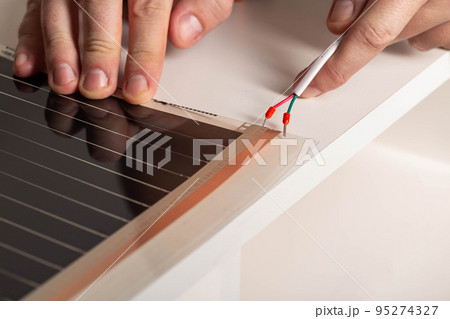 A man connects electric wires to an infrared warm floor. Installation of electric floor heating, macro 95274327