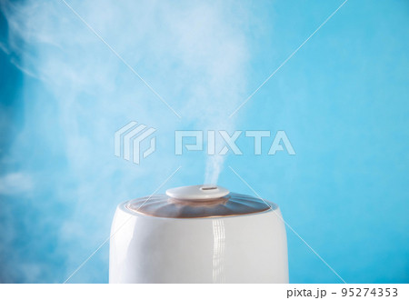 White wet steam from a humidifier on a blue background. Device for healthy air in the room, close-up White wet steam from a humidifier on a blue background. Device for healthy air in the room, close-up 95274353