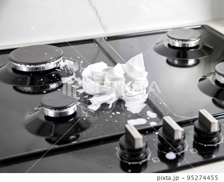 A dirty cloth with a cleaning agent lies on a gas hob. Care and cleaning of grease on a gas stove. Modern kitchen 95274455