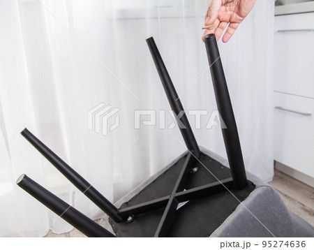 A man glues protective pads on the legs of a chair. Protection against floor scratches and noise A man glues protective pads on the legs of a chair. Protection against floor scratches and noise 95274636