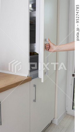 A man opens the door of a built-in refrigerator in the kitchen. Modern refrigerator placement technologies, renovation A man opens the door of a built-in refrigerator in the kitchen. Modern refrigerator placement technologies, renovation 95274785