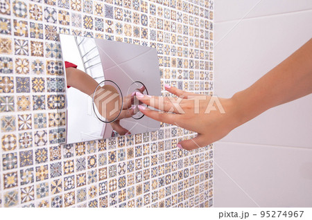a woman's hand presses the flush button of the toilet cistern with installation, close-up 95274967