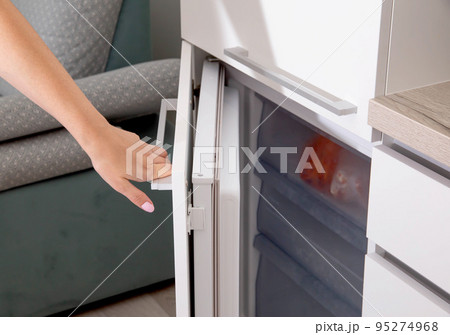 A woman's hand opens the door of the built-in freezer in a modern white kitchen, close-up A woman's hand opens the door of the built-in freezer in a modern white kitchen, close-up 95274968