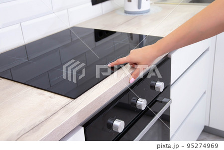 Modern induction hob in the kitchen. A woman's hand sets the heating power of the burner, ceramic 95274969