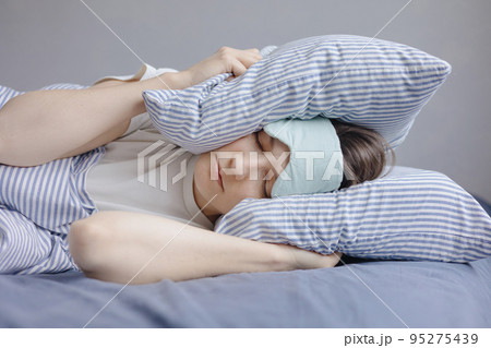 woman is sleeping in bed and covers her head with pillows from noise and light. the woman suffers from insomnia woman is sleeping in bed and covers her head with pillows from noise and light. the woman suffers from insomnia 95275439