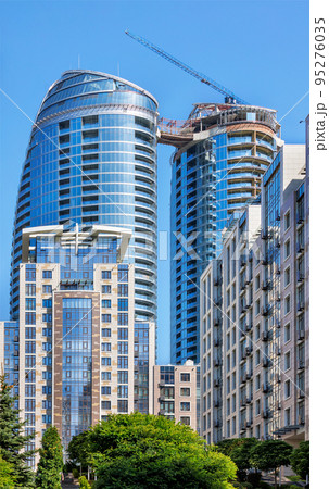 Glass facade of a modern multi-storey residential building under construction against a blue background of the summer sky. Glass facade of a modern multi-storey residential building under construction against a blue background of the summer sky. 95276035