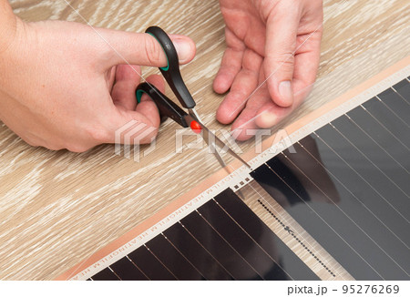 A man cuts an infrared film for a warm floor with scissors. Installation of a warm floor, close-up A man cuts an infrared film for a warm floor with scissors. Installation of a warm floor, close-up 95276269