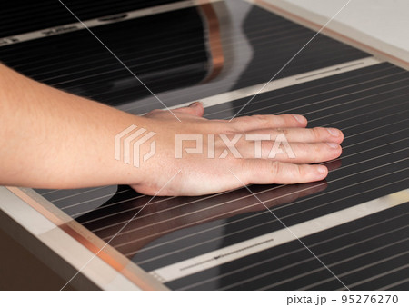 A man checks with his hand the heat from the infrared floor heating after installation. Close-up A man checks with his hand the heat from the infrared floor heating after installation. Close-up 95276270