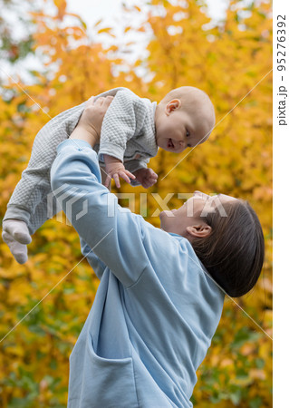 Woman lifts up charmed baby clenching fist in autumn park 95276392