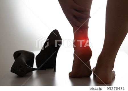 The girl holds on to the inflamed ankle joint, high heels are next to her. Concept of leg joint pain due to uncomfortable shoes 95276481