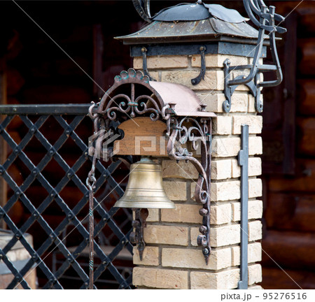 Bronze antique bell hanging at the entrance of the gate to the courtyard of the house, close-up Bronze antique bell hanging at the entrance of the gate to the courtyard of the house, close-up 95276516