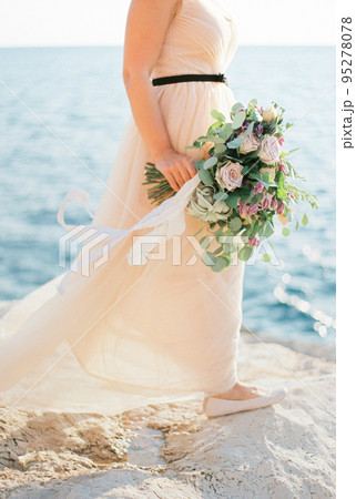 Bouquet of flowers in the bride hand on a stone seashore 95278078
