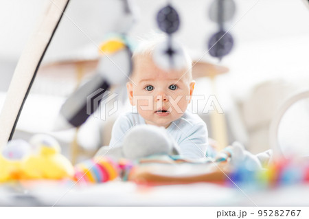Cute baby boy playing with hanging toys arch on mat at home Baby activity and play center for early infant development. Baby playing at home Cute baby boy playing with hanging toys arch on mat at home Baby activity and play center for early infant development. Baby playing at home 95282767