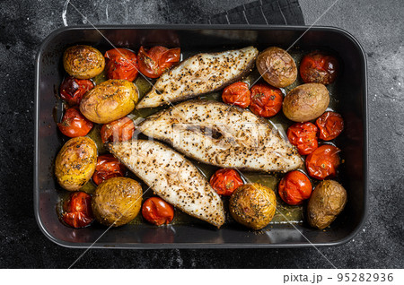 Roasted halibut fish steaks with tomato and potato. Black background. Top view 95282936