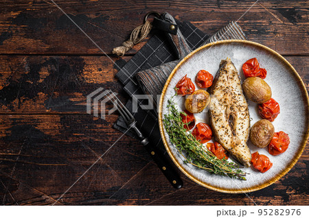 Grilled halibut fish steaks with tomato and potato in plate. Wooden background. Top view. Copy space 95282976