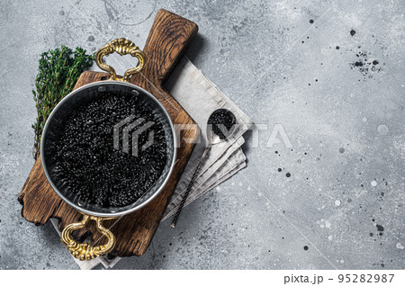 Luxury skillet with Black caviar on wooden board. Gray background. Top view. Copy space 95282987