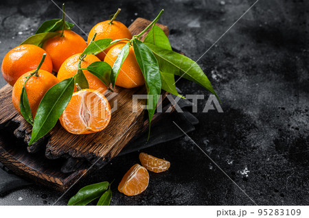 Mandarin oranges or tangerines fruits with leaves on wooden board. Black background. Top view. Copy space Mandarin oranges or tangerines fruits with leaves on wooden board. Black background. Top view. Copy space 95283109