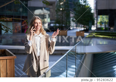 Corporate woman having a phone call on an empty street in business center. Businesswoman having a conversation on telephone while standing outside Corporate woman having a phone call on an empty street in business center. Businesswoman having a conversation on telephone while standing outside 95283622