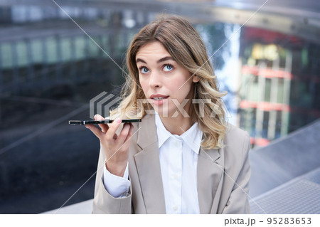 Young office girl talking on mobile phone, recording voice message, holding smartphone near mouth 95283653
