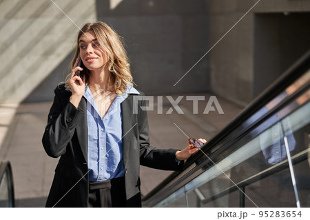 Smiling successful business woman talking on mobile phone while going up on escalator, walking in city Smiling successful business woman talking on mobile phone while going up on escalator, walking in city 95283654