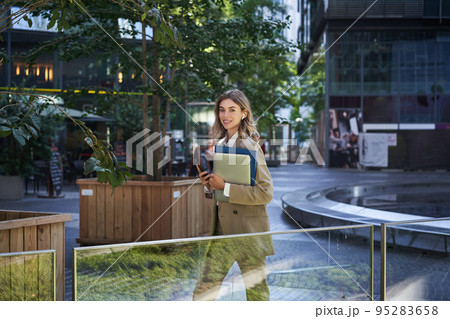 Beautiful smiling woman dressed in corporate suit, holding laptop and documents, smiling at camera 95283658