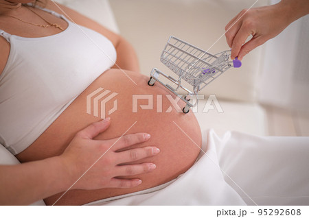 Faceless pregnant woman with shopping cart on her belly.  95292608