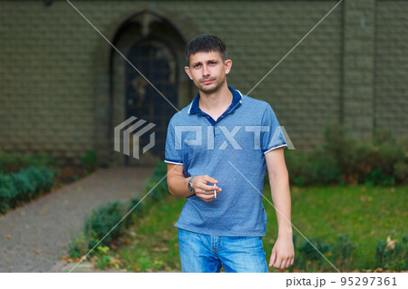 An unshaven man stands on street smoking in anticipation something in thought An unshaven man stands on street smoking in anticipation something in thought 95297361