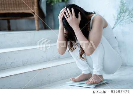 体重を計ってショックを受ける若い女性 95297472