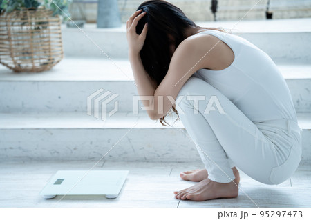 体重を計ってショックを受ける若い女性 95297473
