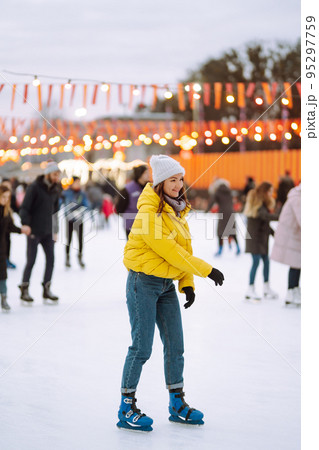 Happy woman ice skating on the ice arena in the city square on Festive Christmas fair. Cold weather. Happy woman ice skating on the ice arena in the city square on Festive Christmas fair. Cold weather. 95297759