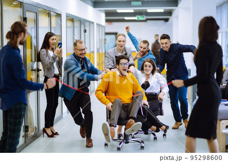 Young colleagues group having fun together, riding on chairs in office 95298600