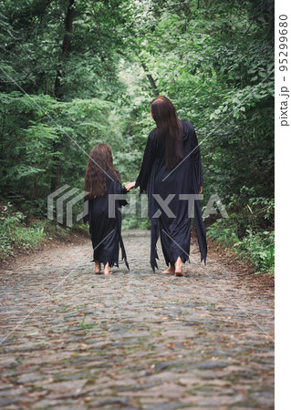 A young witch and her daughter are walking through a forest A young witch and her daughter are walking through a forest 95299680