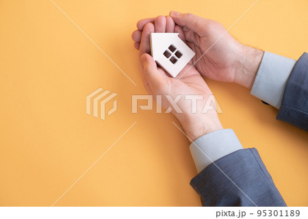 Man holding a small wooden house in the hand isolated of yellow background Man holding a small wooden house in the hand isolated of yellow background 95301189