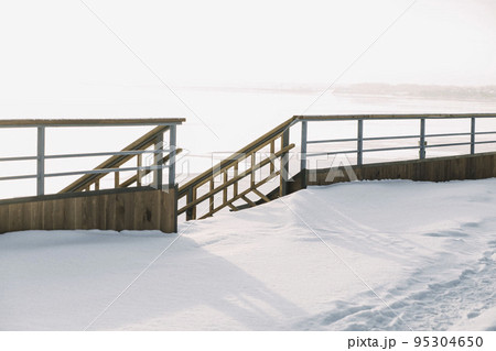 Outdoor wooden downstairs with stair railings in wintertime with a lot of snow, terrace and railings overlooking the lake Outdoor wooden downstairs with stair railings in wintertime with a lot of snow, terrace and railings overlooking the lake 95304650
