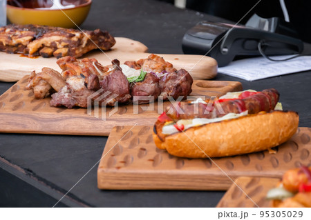 Hot dog, beef ribs and shish kebab on wooden board at street food festival Hot dog, beef ribs and shish kebab on wooden board at street food festival 95305029