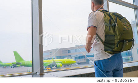 a male traveler with a backpack on his back is waiting for landing on the background of an airplane. Travel concept. Aircraft preparation before takeoff. a male traveler with a backpack on his back is waiting for landing on the background of an airplane. Travel concept. Aircraft preparation before takeoff. 95305367