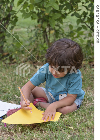 Young Caucasian school boy sitting in park outdoor doing school homework. Child kid writing in notebook with pencil outside. Self education learning studying. Early development for children. Young Caucasian school boy sitting in park outdoor doing school homework. Child kid writing in notebook with pencil outside. Self education learning studying. Early development for children. 95305895