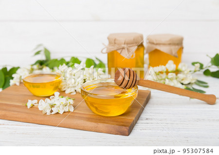 Sweet honey jar surrounded spring acacia blossoms. Honey flows from a spoon in a jar. jars of clear fresh acacia honey on wooden background 95307584