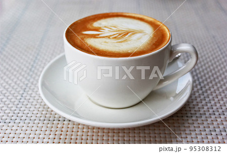 Hot art latte coffee in a cup on a white table Hot art latte coffee in a cup on a white table 95308312