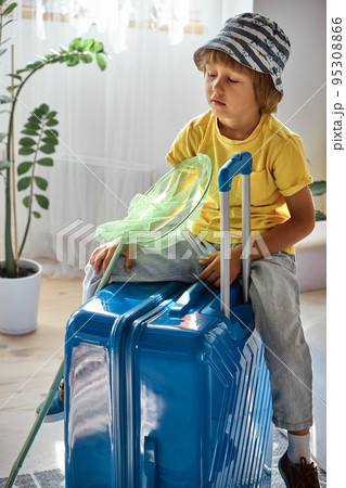 A sad child sits on a suitcase and waits for departure. Family relocation, flight from the country A sad child sits on a suitcase and waits for departure. Family relocation, flight from the country 95308866