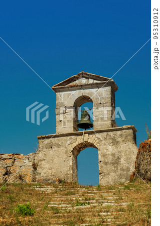 Decayed stone built bell tower with hanging bronze bell on top of a hill. Decayed stone built bell tower with hanging bronze bell on top of a hill. 95310912