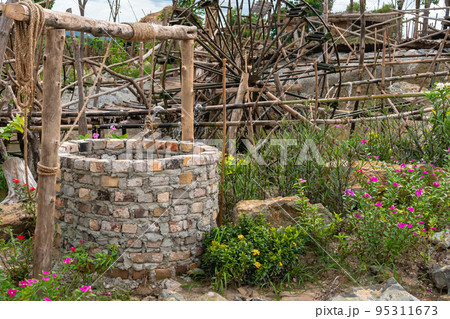 Beautiful artesian well made by bricks with cement and wheel pulley with metal bucket and rope in peaceful garden atmosphere. Retro stone water well in rural area.Garden decoration with antique items 95311673