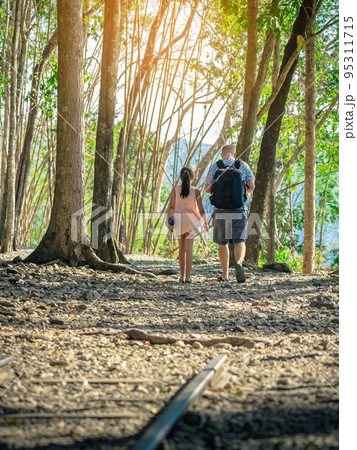 Back view of male tourist and his daughter walking together in forest nature path walk on trail woods background at Hellfire Pass in Kanchanaburi Thailand. Happy people relaxing on active outdoor. 95311715