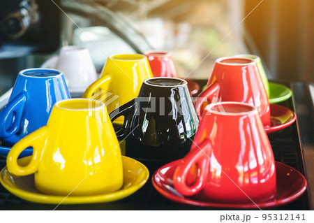 Close up to colorful ceramic upside down coffee cups on coffee machine in cafe. Multi colored upside down the coffee cups in coffee shop. Group of color tea or coffee cups. Selective Focus. Close up to colorful ceramic upside down coffee cups on coffee machine in cafe. Multi colored upside down the coffee cups in coffee shop. Group of color tea or coffee cups. Selective Focus. 95312141