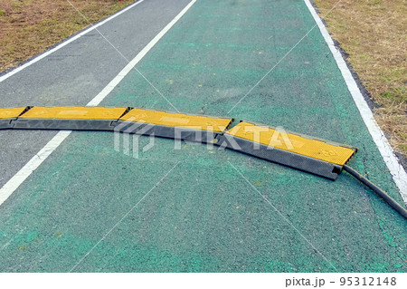 Black and yellow heavy plastic covers for people and vehicle to cross over cables laid on road. Pavement pads to protect electrical wiring on sidewalk in public park. Channel for laying the wires. Black and yellow heavy plastic covers for people and vehicle to cross over cables laid on road. Pavement pads to protect electrical wiring on sidewalk in public park. Channel for laying the wires. 95312148