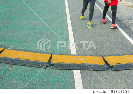 Black and yellow heavy plastic covers for people and vehicle to cross over cables laid on road. Pavement pads to protect electrical wiring on sidewalk in public park. Channel for laying the wires. Black and yellow heavy plastic covers for people and vehicle to cross over cables laid on road. Pavement pads to protect electrical wiring on sidewalk in public park. Channel for laying the wires. 95312150