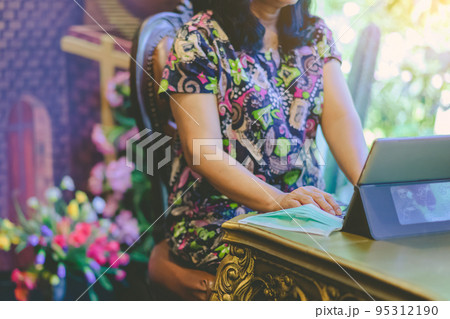Hands of mature woman typing on laptop keyboard to work from home and take off her surgical mask put it on the table for easy breathing. Concepts of Covid-19 (Coronavirus).  Selective focus on hand. 95312190