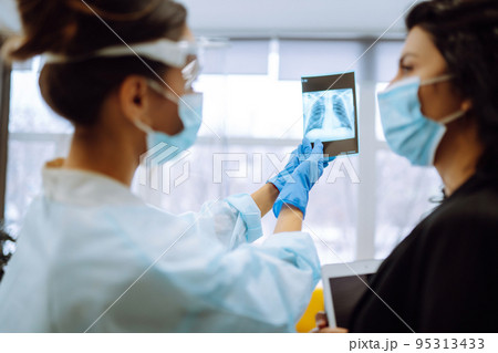 A female doctor in visor and protective gloves discussing an x-ray. Doctor examines an X-ray. A female doctor in visor and protective gloves discussing an x-ray. Doctor examines an X-ray. 95313433