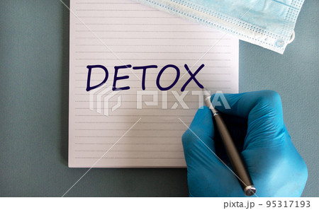 Male doctors hand in blue glove writes the word 'detox' on a white note. Medicine mask. Beautiful blue background. 95317193